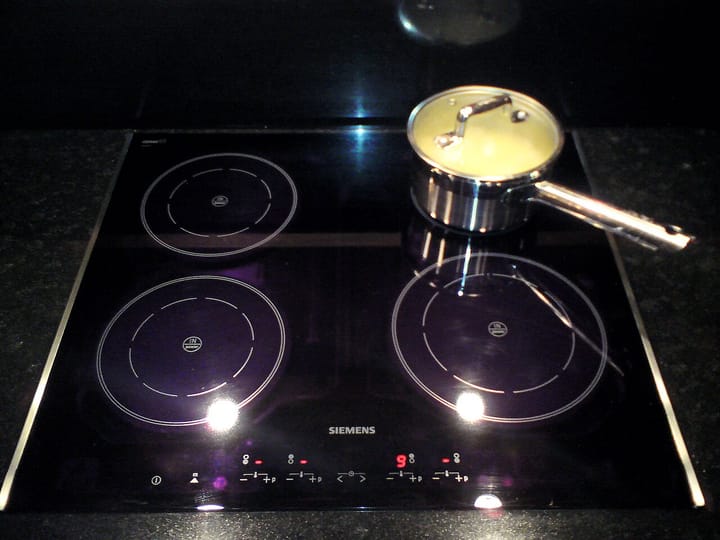 A modern black-glass induction cooktop with a stainless-steel saucepan, the kind of appliance subsidised by Portugal's E-Lar scheme