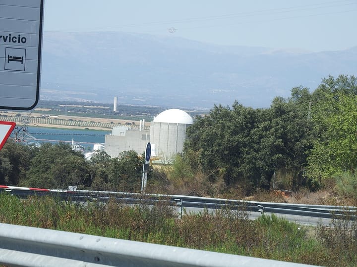 The white domed reactor and grey buildings of the Almaraz Nuclear Power Plant beside a reservoir in Caceres, Spain, seen from a nearby road with hills behind
