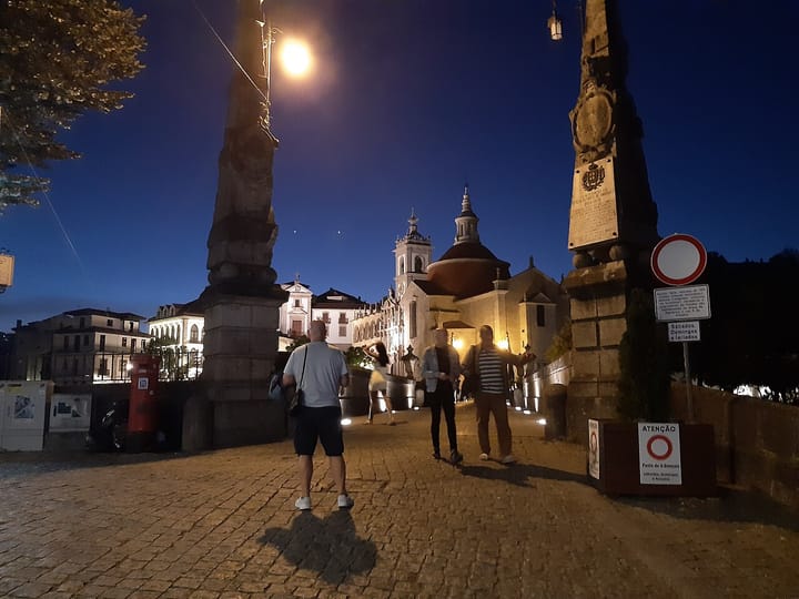 The Ponte de Sao Goncalo stone bridge over the Tamega river in Amarante, Portugal, at dusk, with the illuminated Sao Goncalo church and its dome behind