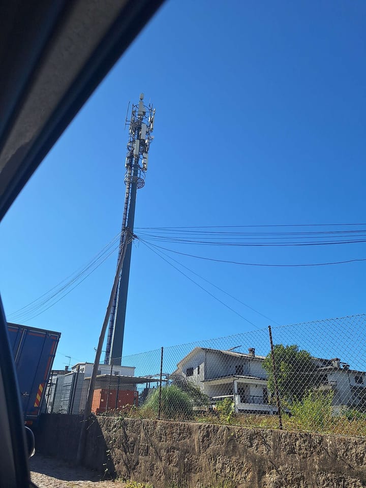 A tall mobile-telecommunications antenna mast rising above suburban houses in northern Portugal under a clear blue sky