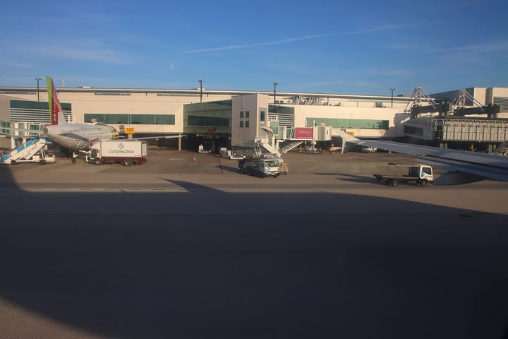 A TAP Air Portugal aircraft parked at a jet bridge on the apron of Lisbon's Humberto Delgado Airport under a clear blue sky
