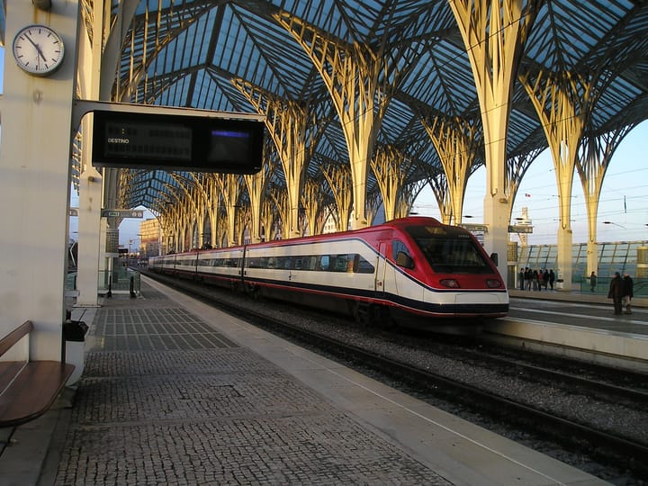 A red and white CP Alfa Pendular train waiting at a platform beneath the tree-like steel canopy of Lisbon's Oriente station