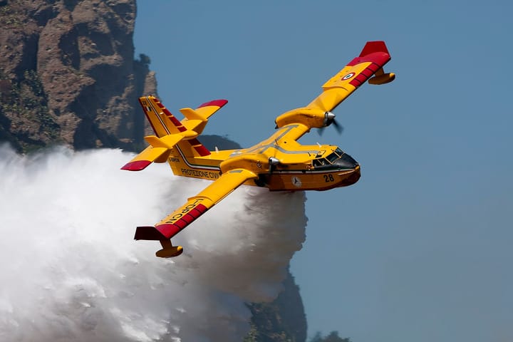 A yellow Italian Civil Protection Canadair firefighting aircraft dropping a plume of water over a hillside, illustrating the aerial reinforcements sent to Portugal