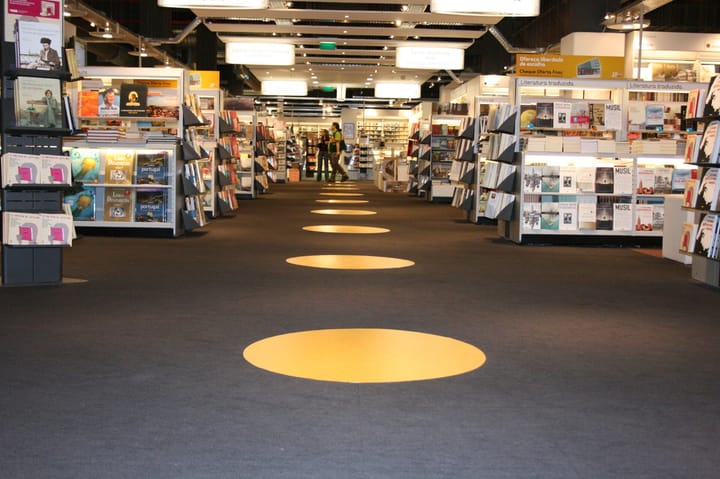 The interior of a Fnac store in Portugal, with aisles of Portuguese-language books and a large yellow circle on the dark carpet