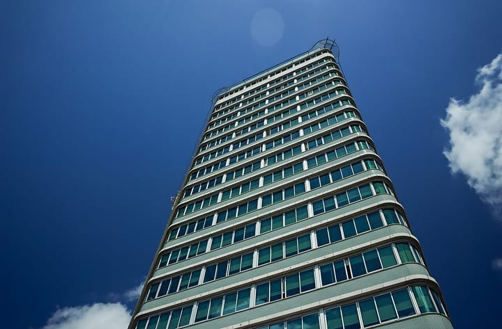 The green-glass tower of the Ministerio do Trabalho e Seguranca Social at Praca de Londres in Lisbon, seen from below against a blue sky