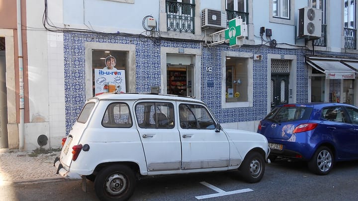A neighbourhood pharmacy with a green cross sign and an azulejo-tiled facade in Lisbon