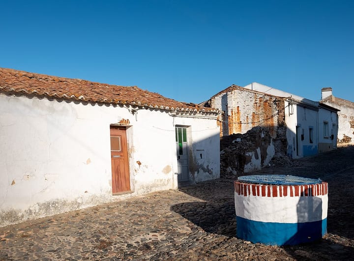 An old whitewashed water well, capped with a metal grille, standing in a cobbled street of Torrao in Alcacer do Sal, Alentejo