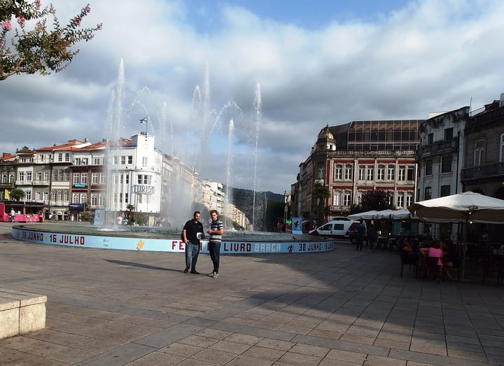 Praca da Republica in Braga, with the square's fountain jets playing, the white Turismo building and the tiled facades of the old town under a cloudy sky
