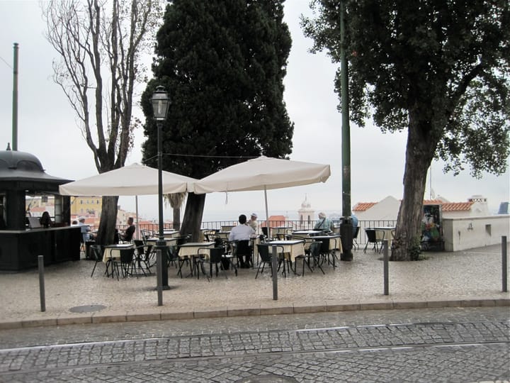 Diners at an outdoor cafe esplanade at a Lisbon miradouro overlooking the city's rooftops