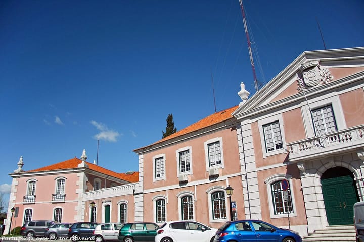 The pink neoclassical wings of the Camara Municipal de Oeiras in Portugal, with the town coat of arms carved into the pediment above the main doorway.