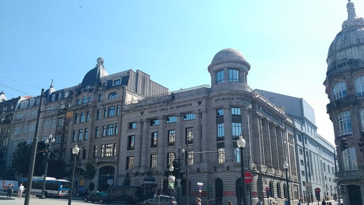 A grand stone Caixa Geral de Depositos bank building in Porto, Portugal, with the bank's name and 'Republica Portuguesa' carved across its facade beneath a domed corner tower