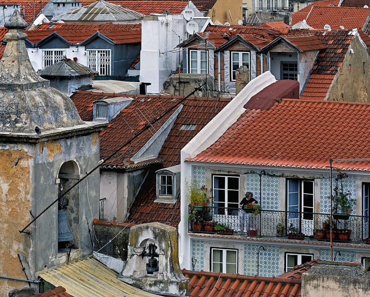 Terracotta rooftops of Lisbon's Chiado quarter, with a resident tending flowers on a tiled balcony among the tightly packed old apartment buildings