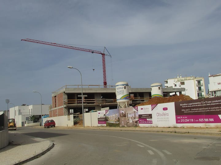 A building site in Albufeira, Portugal, with a red tower crane and the concrete shell of an apartment block under construction