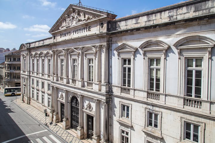 The neoclassical facade of the Tribunal da Relacao de Coimbra, inscribed DOMVS IVSTITIAE, seen from above a Coimbra street.