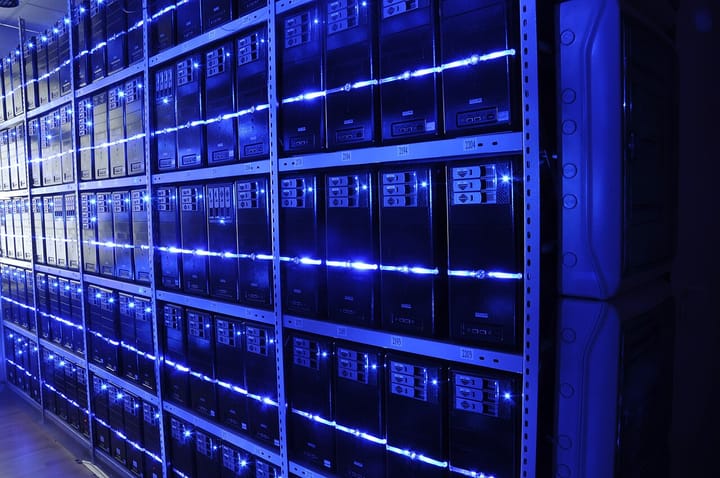 Rows of servers glowing with blue LED lights inside a data centre, seen down a long aisle of racks