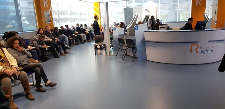 Members of the public seated in a long row waiting at the Balcao dos Registos service counter in the Campus de Justica in Lisbon, with staff at the curved desk