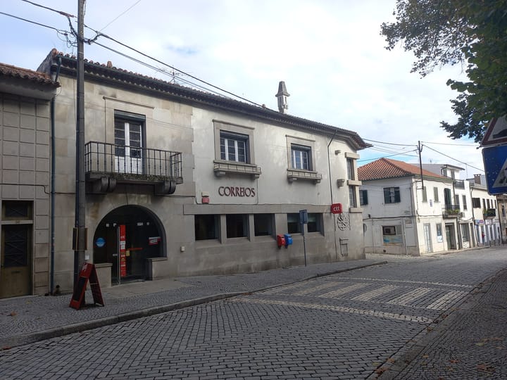 The stone Correios post office building with a red ctt sign on a cobbled street in Nelas, Viseu district, Portugal, under a blue sky.