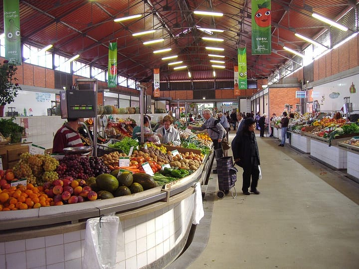 Shoppers browsing fruit and vegetable stalls piled with oranges, grapes and melons inside the municipal market hall in Olhão, in Portugal's Algarve
