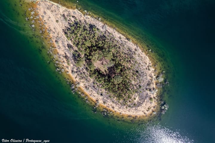 Aerial view of a scorched, part-burned island in the Barragem de Santa Luzia reservoir in central Portugal, ringed by exposed shoreline