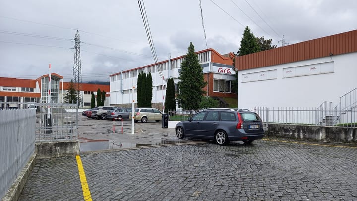 The white and orange factory buildings and gated car park of the Ara Shoes Portuguesa footwear plant at Seia in central Portugal on an overcast day.