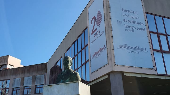 The Hospital Professor Doutor Fernando Fonseca in Amadora, known as Amadora-Sintra, with banners on its facade and a bronze bust of Fernando Fonseca in the foreground