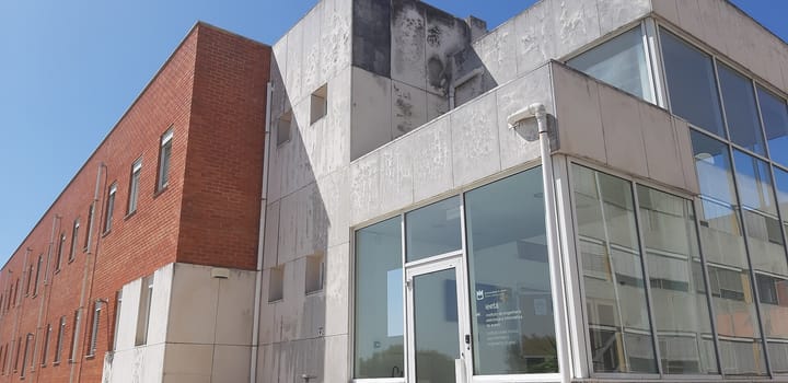 The glass entrance of the Instituto de Engenharia Eletronica e Informatica de Aveiro, a brick and concrete research building at the University of Aveiro, under a clear blue sky.