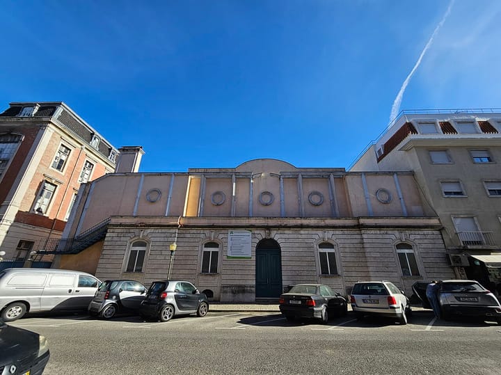 The Instituto do Emprego e Formacao Profissional employment centre in Alcantara, Lisbon, a low stone-fronted building with arched windows, cars parked along the street under a clear sky