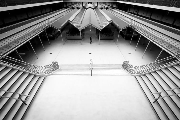 The rebuilt Mercado do Bolhao in Porto seen from the upper gallery in black and white, its rows of pitched stall roofs almost empty, a single figure crossing the central aisle.