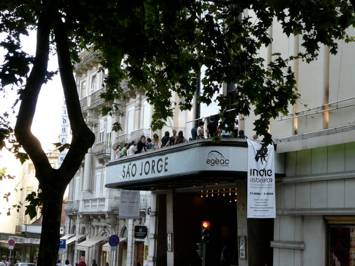 The facade of Cinema Sao Jorge on Avenida da Liberdade in Lisbon, its lettered marquee framed by plane trees, with a film festival banner hanging beside the entrance