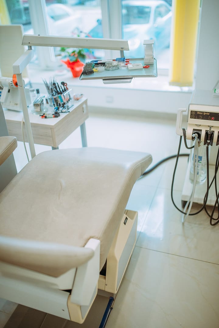 An empty modern dental treatment chair with an overhead lamp, instrument tray and equipment in a bright clinic