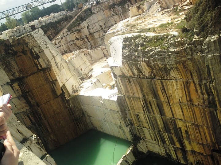 A deep open-pit marble quarry with white and beige stone walls and green water pooled at the bottom, in the Estremoz marble belt of the Alentejo, Portugal