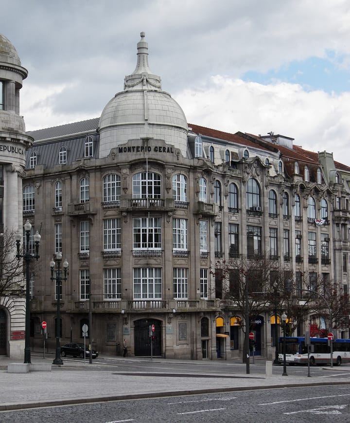 The grey stone Montepio Geral building in central Porto, its name carved beneath a domed corner tower