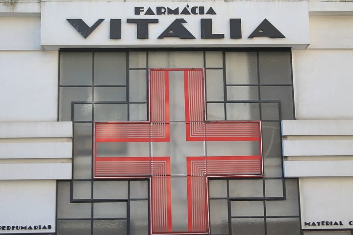 The facade of a Portuguese pharmacy showing the word Farmacia and a large red pharmacy cross