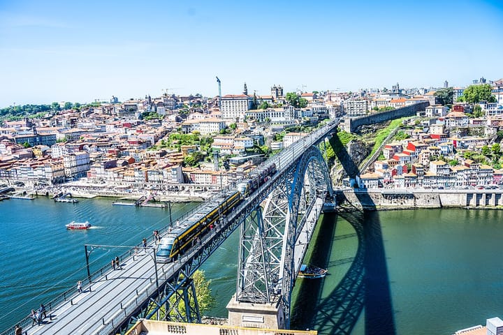 Aerial view of Porto, Portugal, with a yellow metro train crossing the double-deck Dom Luis I bridge over the Douro river and the historic old town behind