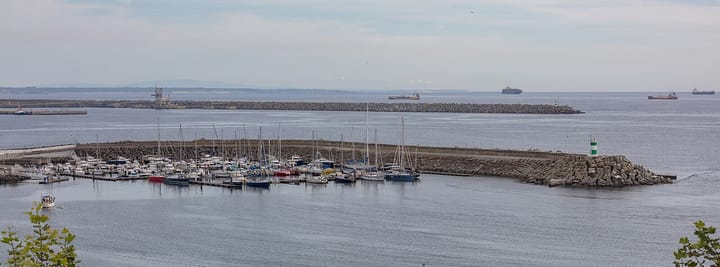Cargo ships anchored beyond the breakwaters at the port of Sines, with yachts moored inside the marina in the foreground