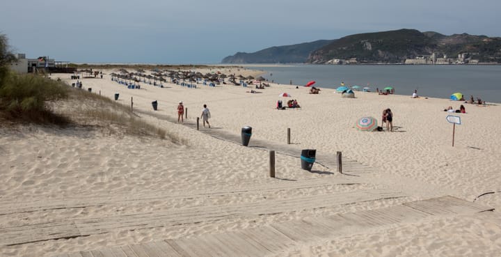 Sandy beach on the Tróia peninsula with thatched sun umbrellas, the Sado estuary and the Arrábida hills near Setúbal, Portugal