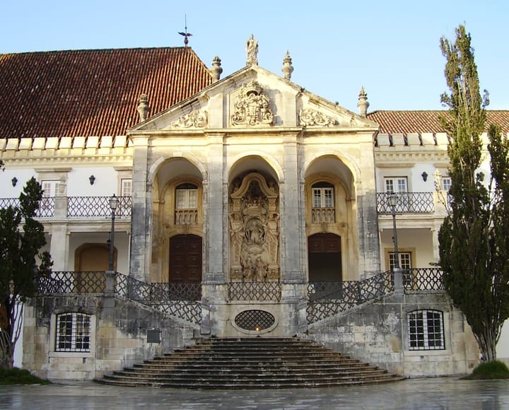 The ornate baroque stone main entrance of the University of Coimbra, flanked by twin staircases in the old university courtyard
