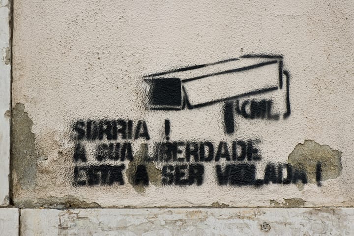 A Lisbon street stencil of a surveillance camera reading Sorria, a sua liberdade esta a ser vigiada