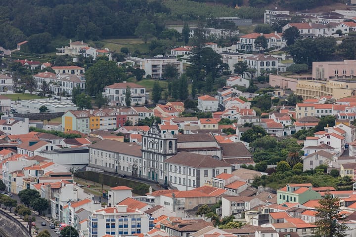 An aerial view over the red tiled roofs and white houses of Horta on Faial in the Azores, with the stone facade of the former Jesuit college and its church at the centre.