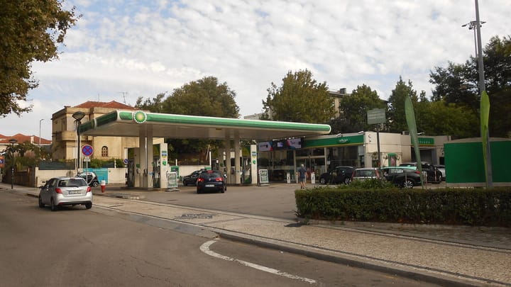 A BP filling station on a street corner in Paranhos, Porto, its green canopy over four pump islands, with cars queuing at the forecourt and a shop building behind.