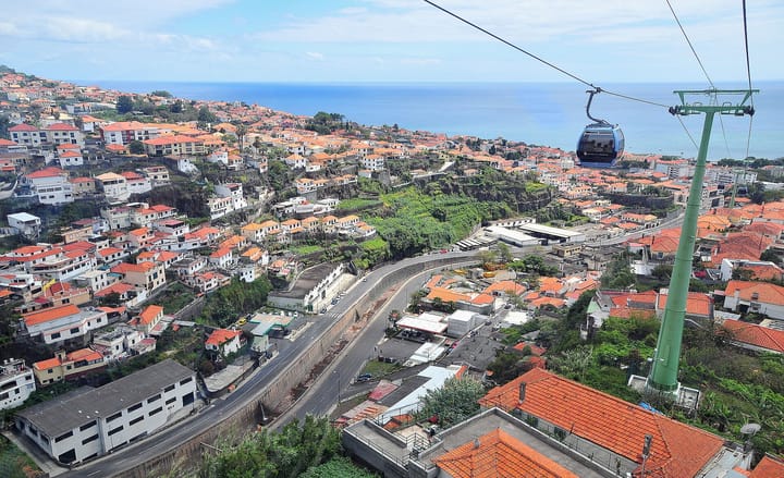 A cable-car gondola above the red-tiled rooftops of Funchal, Madeira, descending toward the blue Atlantic on a sunny day