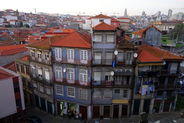 A view over the blue-tiled facades and terracotta rooftops of central Porto, with the wider city skyline and a tower in the distance