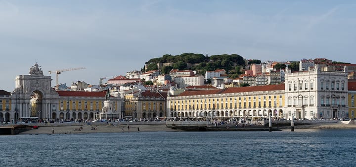 The Praca do Comercio waterfront in Lisbon seen from the Tagus, with the Arco da Rua Augusta, its yellow arcades and the Castelo de Sao Jorge on the hill behind