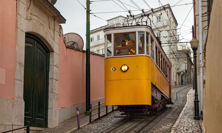 A yellow Elevador da Glória funicular carriage climbing the cobbled Calçada da Glória between pastel buildings in central Lisbon