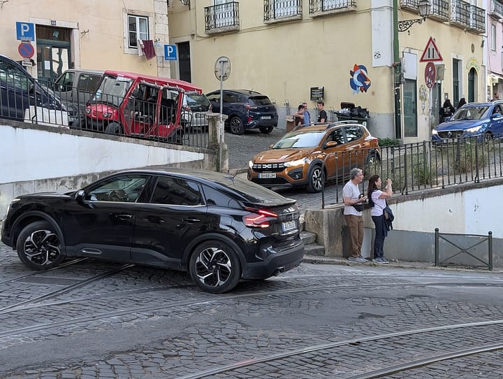 Cars parked and driving on a cobbled street in the Alfama district of Lisbon, with tram tracks in the road and traditional Portuguese buildings behind, illustrating Portugal's vehicle fleet