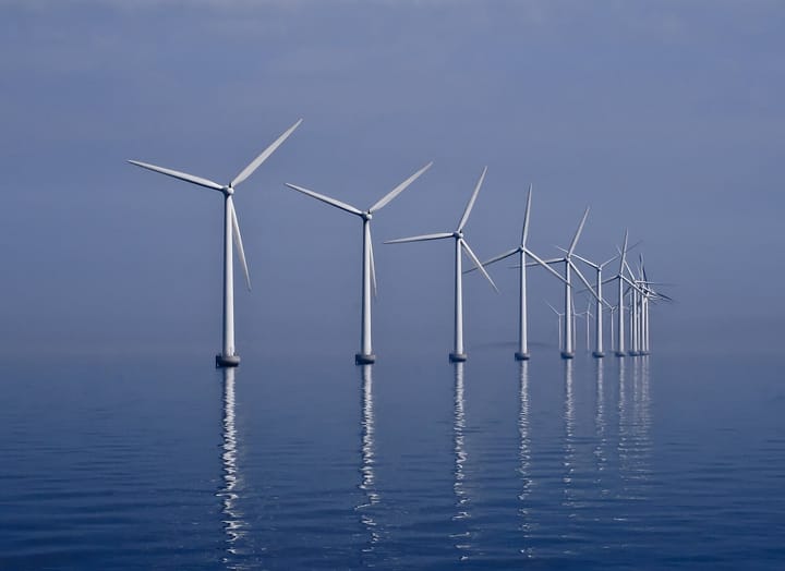 A row of offshore wind turbines standing in calm sea under a hazy blue sky