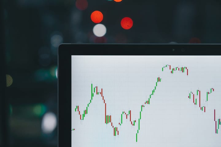 A laptop screen showing a green-and-red candlestick stock chart trending higher, city lights blurred behind it