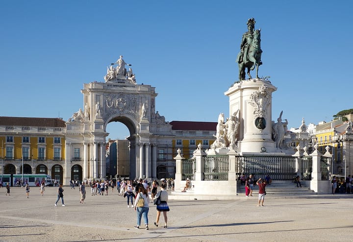 Praca do Comercio in Lisbon on a sunny day, with the Rua Augusta triumphal arch, the equestrian statue of King Jose I and pedestrians crossing the historic riverside square