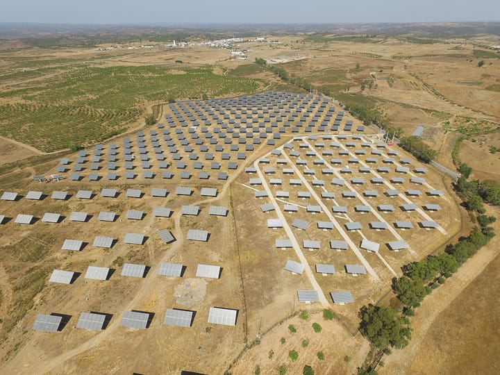 Aerial view of the Alcoutim solar platform in the Algarve interior, rows of photovoltaic panels spread across dry farmland with a village on the horizon