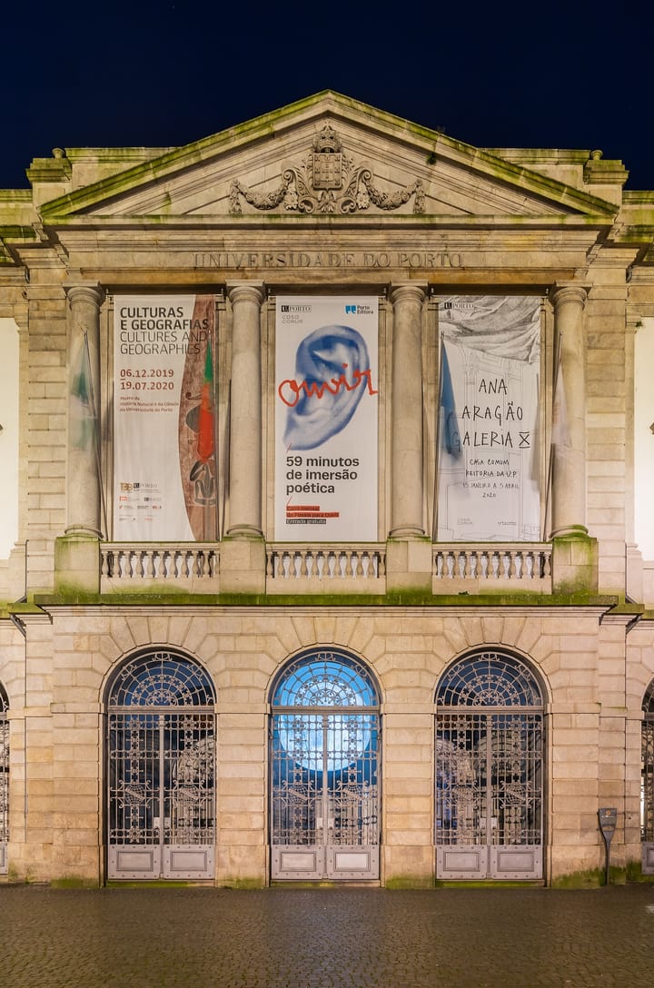 The neoclassical stone facade of the Rectory of the University of Porto, with 'UNIVERSIDADE DO PORTO' carved above its columns, lit at dusk